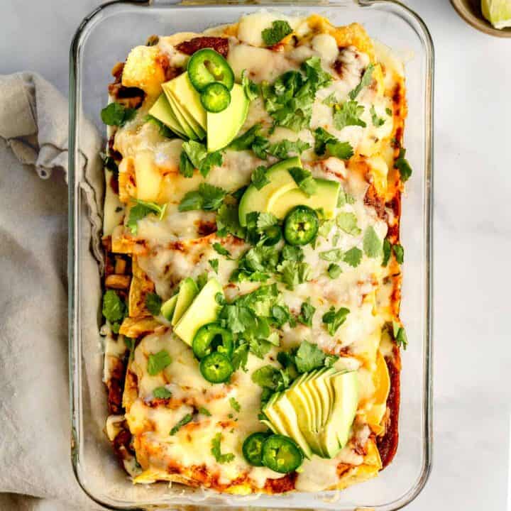 Veggie enchiladas with red sauce in a glass casserole dish.
