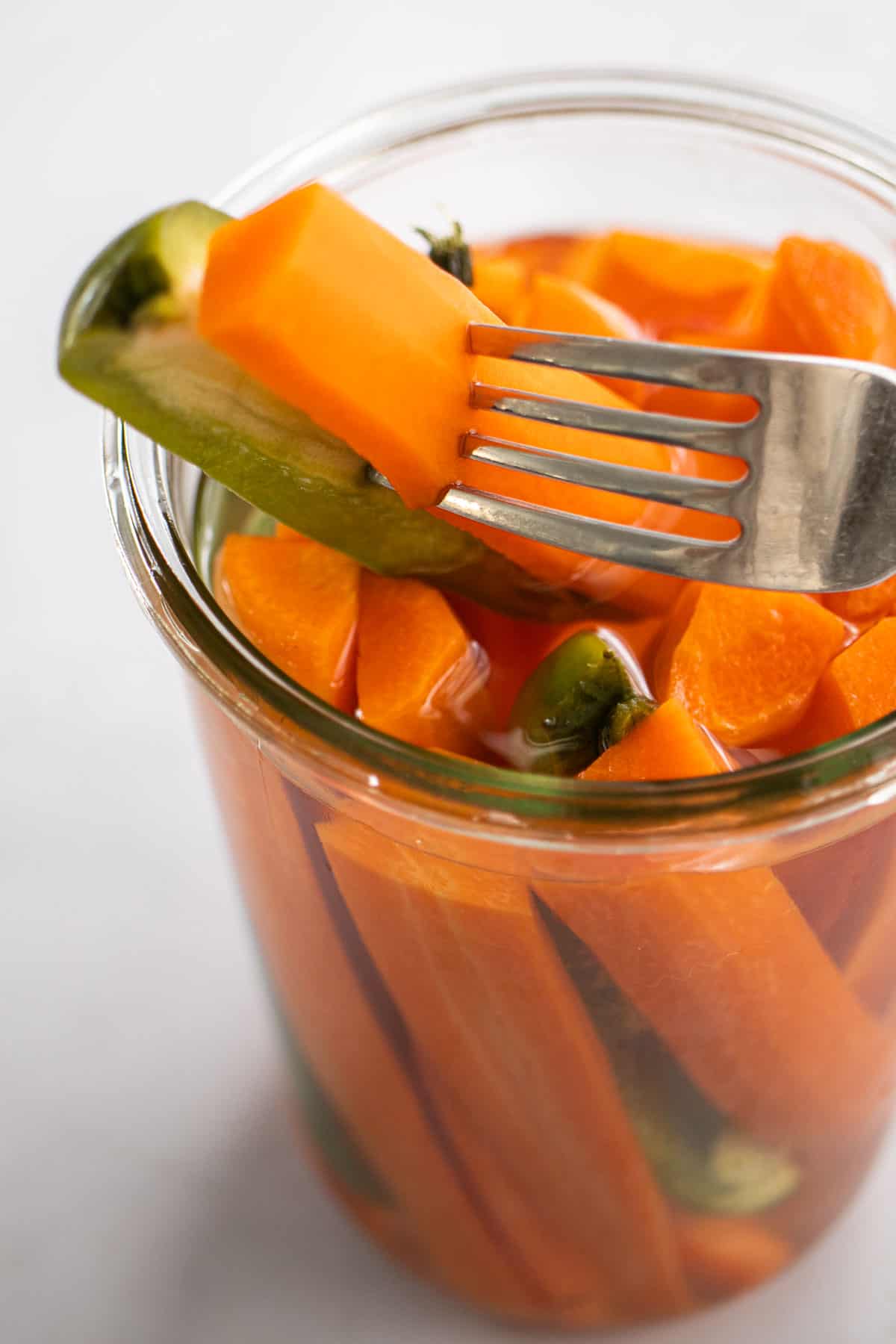 Fork with pickled carrot and jalapeño over the pickle jar.