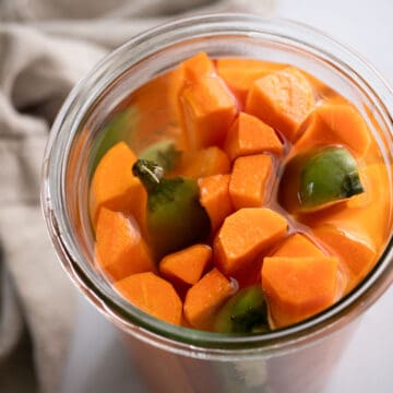 Square image of pickled carrots in a glass jar.