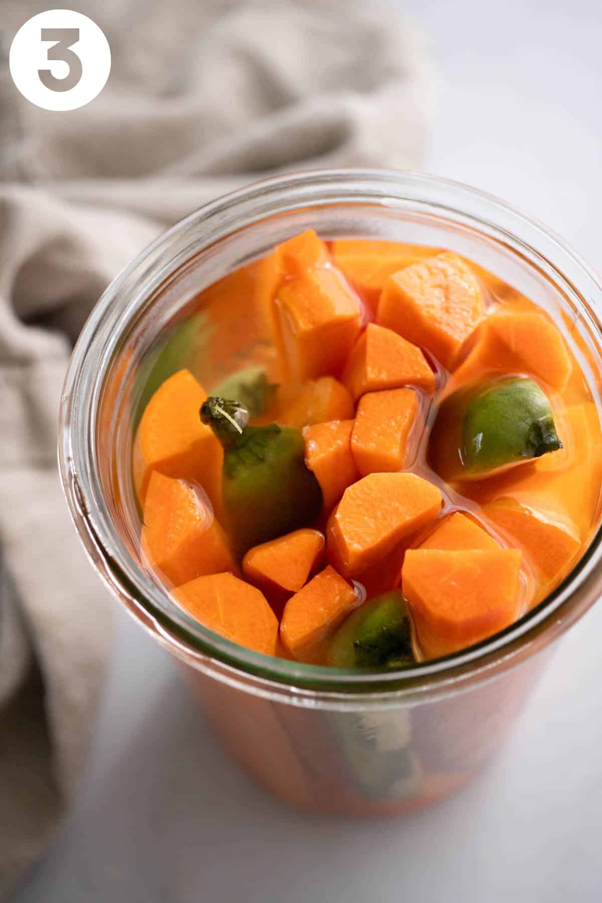 Looking into a jar of quick pickled carrots soaking in brine with jalapeño pepper. Labeled with a 