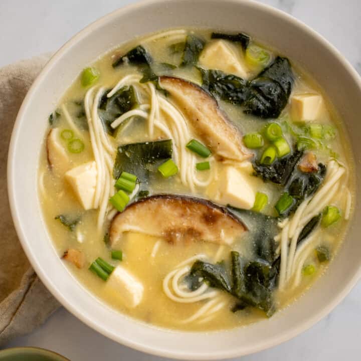 Closeup of vegetarian miso noodle soup with shiitake mushrooms in a white bowl.
