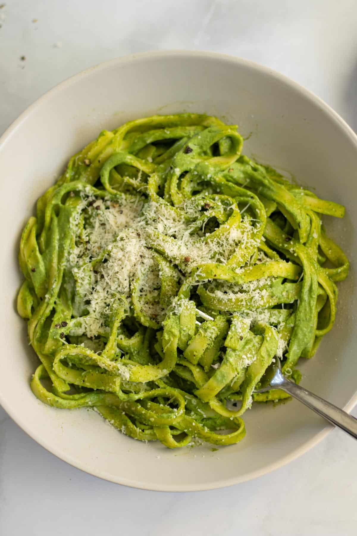 Fettuccine pasta with creamy, green spinach sauce, garnished with freshly grated parmesan cheese and black pepper.