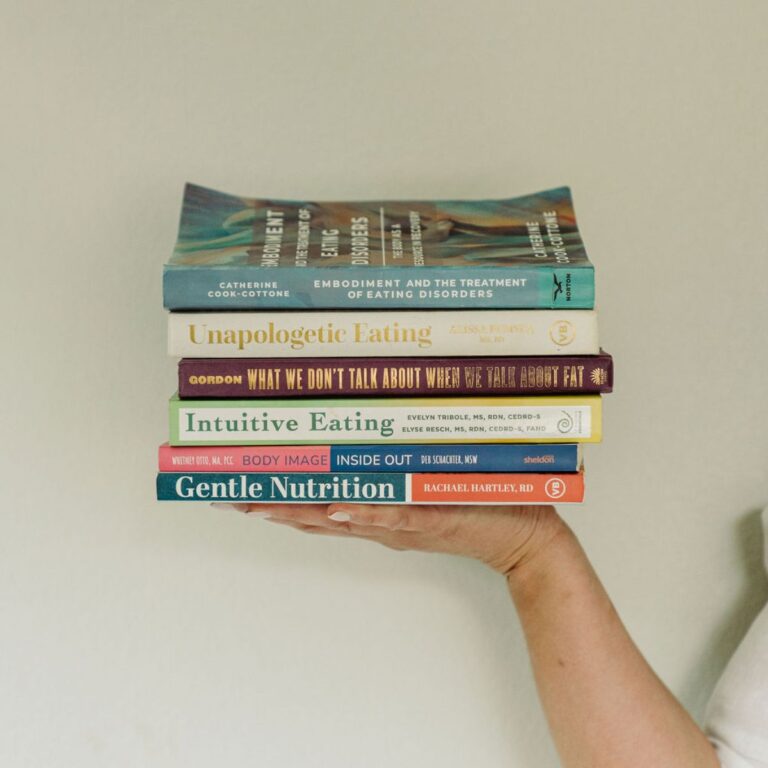 A hand holding a stack of nutrition and intuitive eating books against a white background.