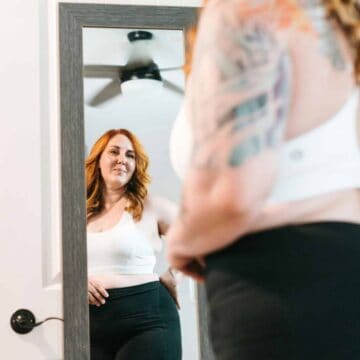 Woman in workout clothes looking in the mirror and smiling.