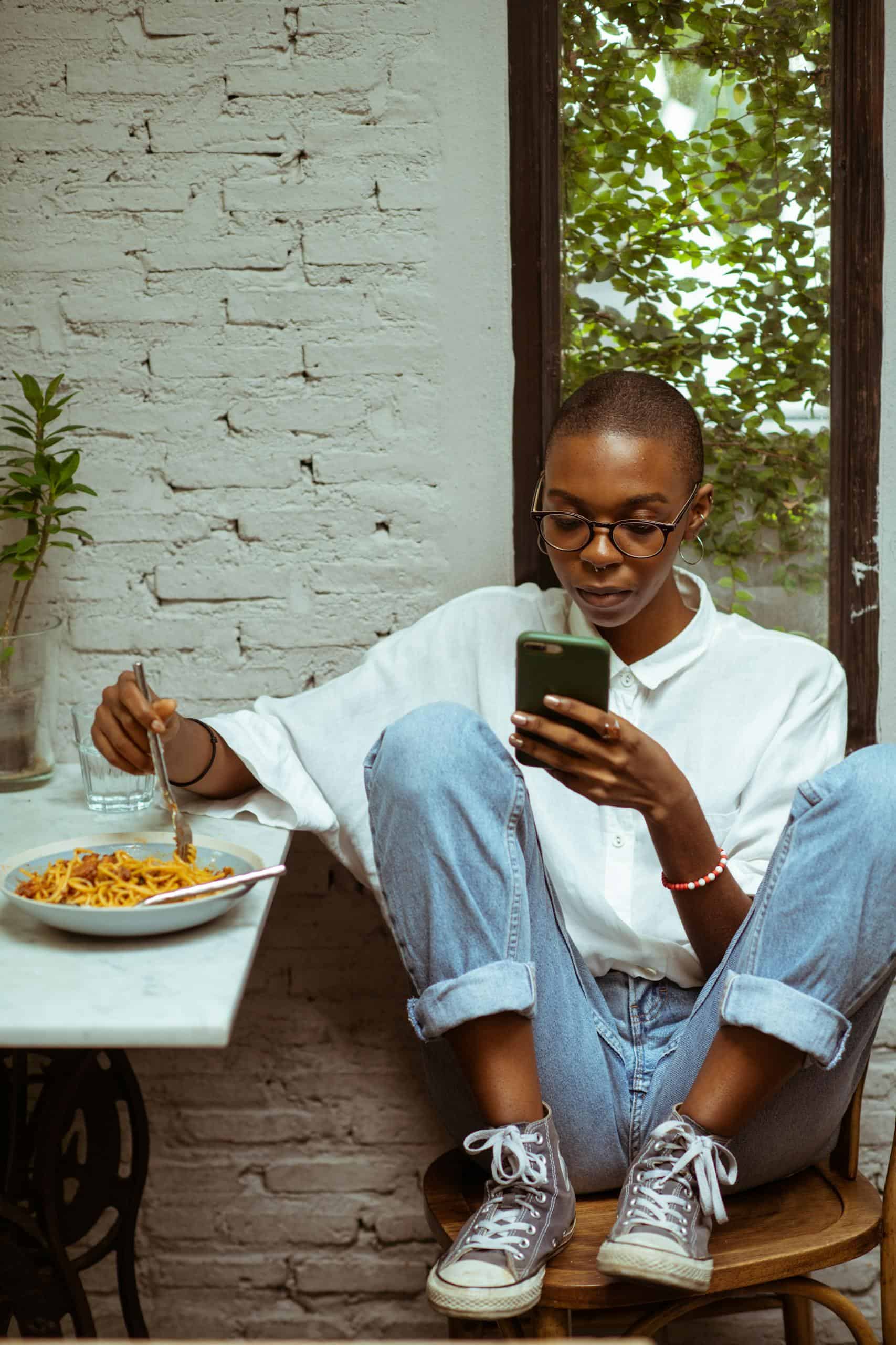 A woman eating pasta while using a food tracking app on her phone.