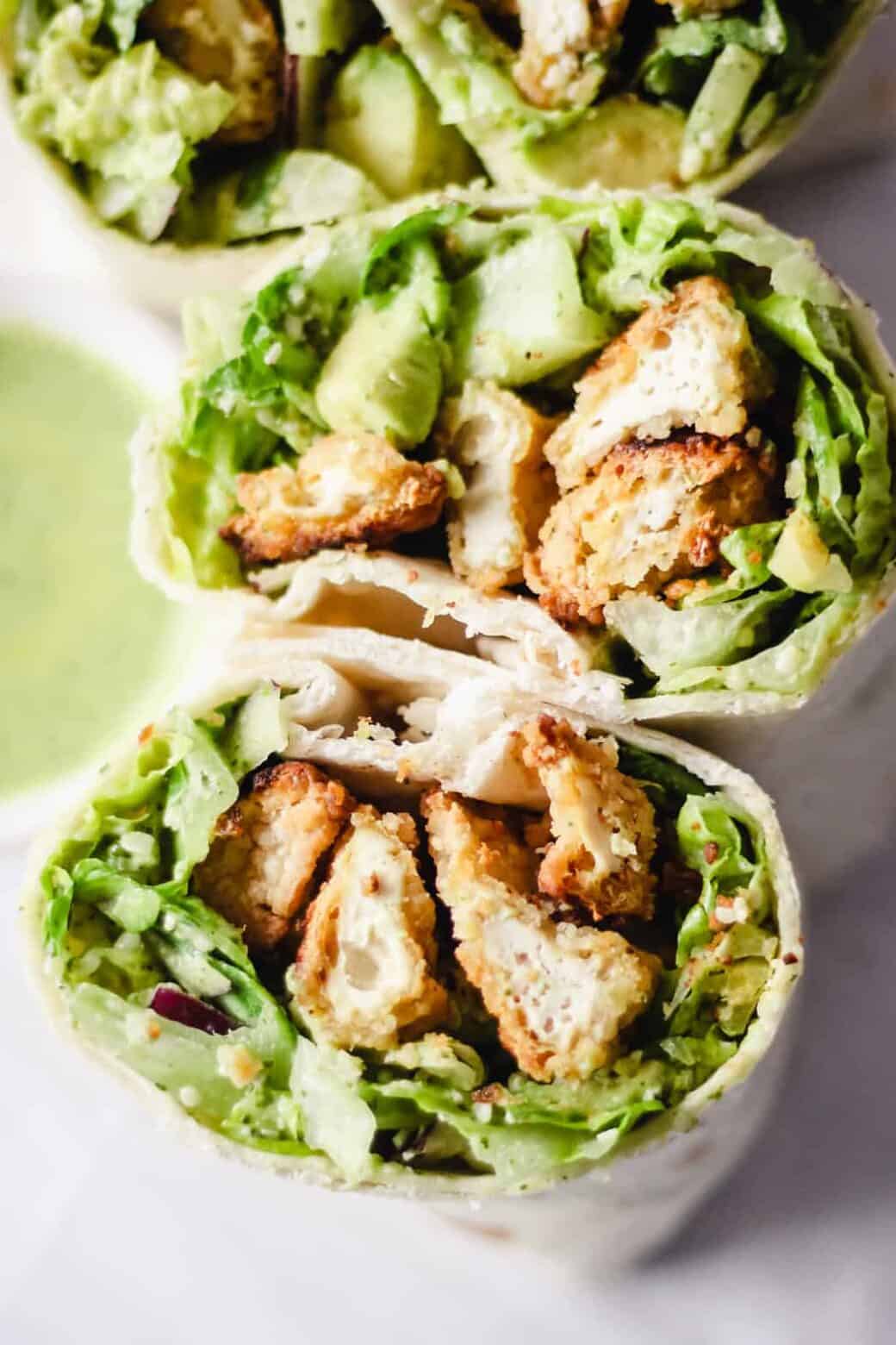 Tofu wrap with lettuce cut in half with a small bowl of green goddess dressing next to it.