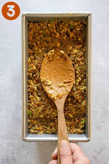 Using a wooden spoon to press the lentil loaf into the baking pan.