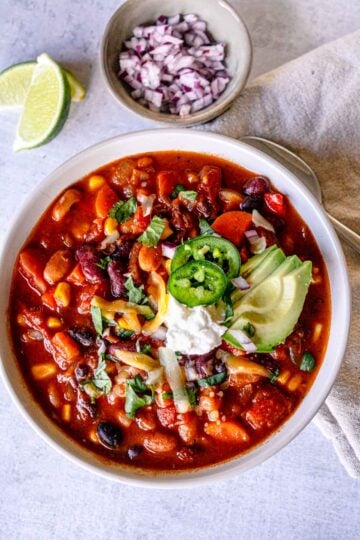 Bowl of vegetarian bean chili with toppings, including avocado, cilantro, and sliced jalapeño.