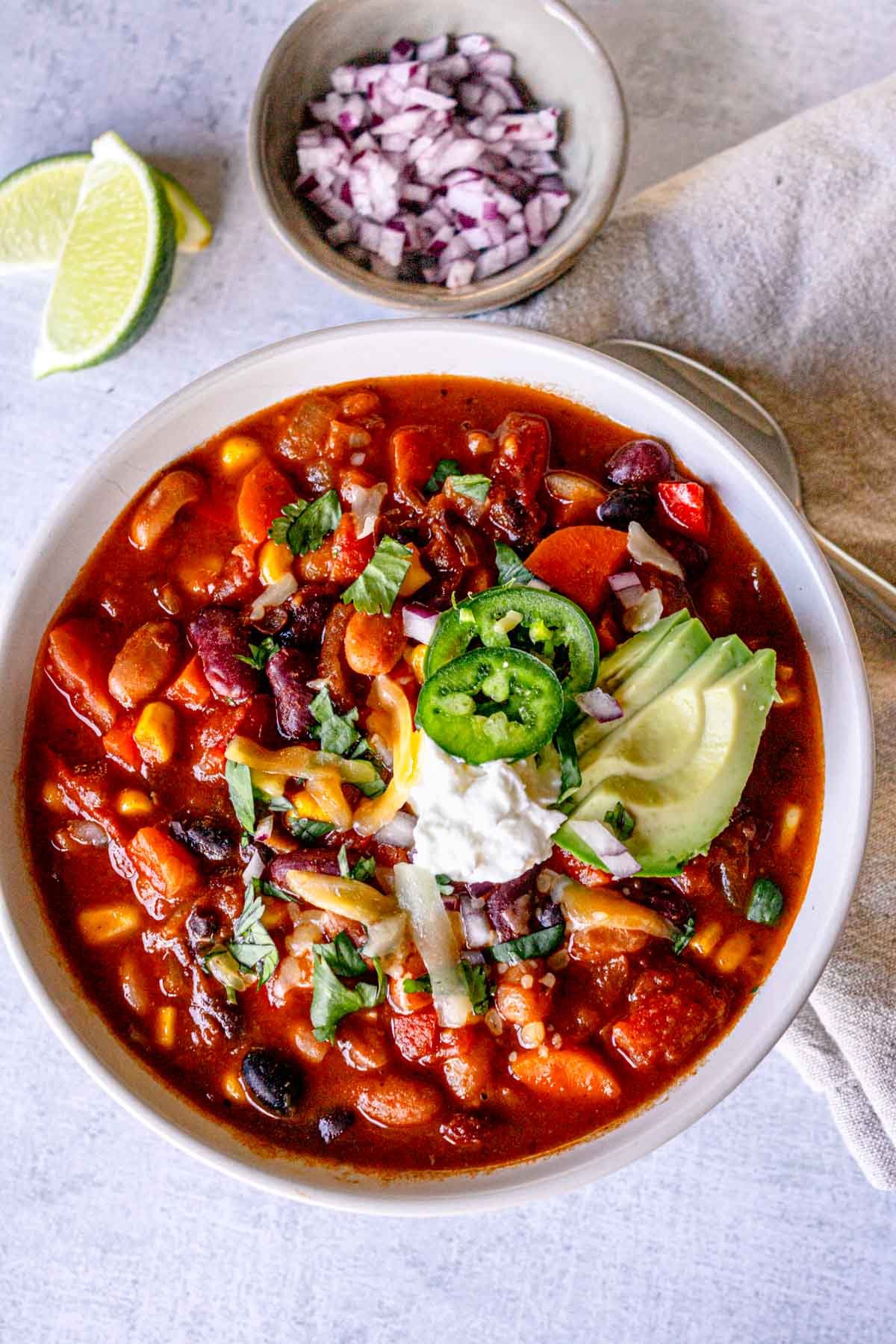 Bowl of vegetarian bean chili with toppings, including avocado, cilantro, and sliced jalapeño.