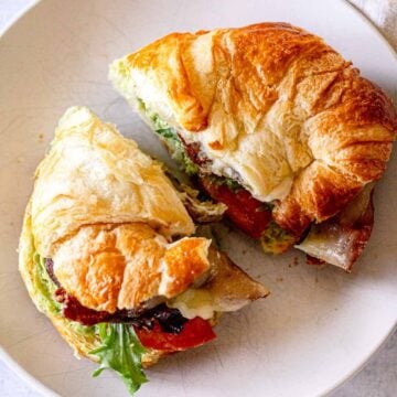 Bacon sandwich on a croissant with melted Swiss cheese, lettuce, tomato, avocado, and mayo.