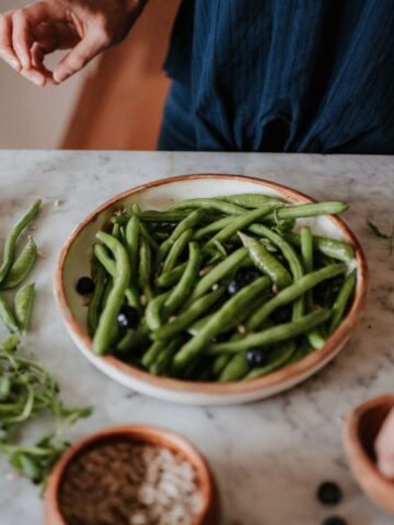 Green beans in a ceramic dish with hands preparing salad.