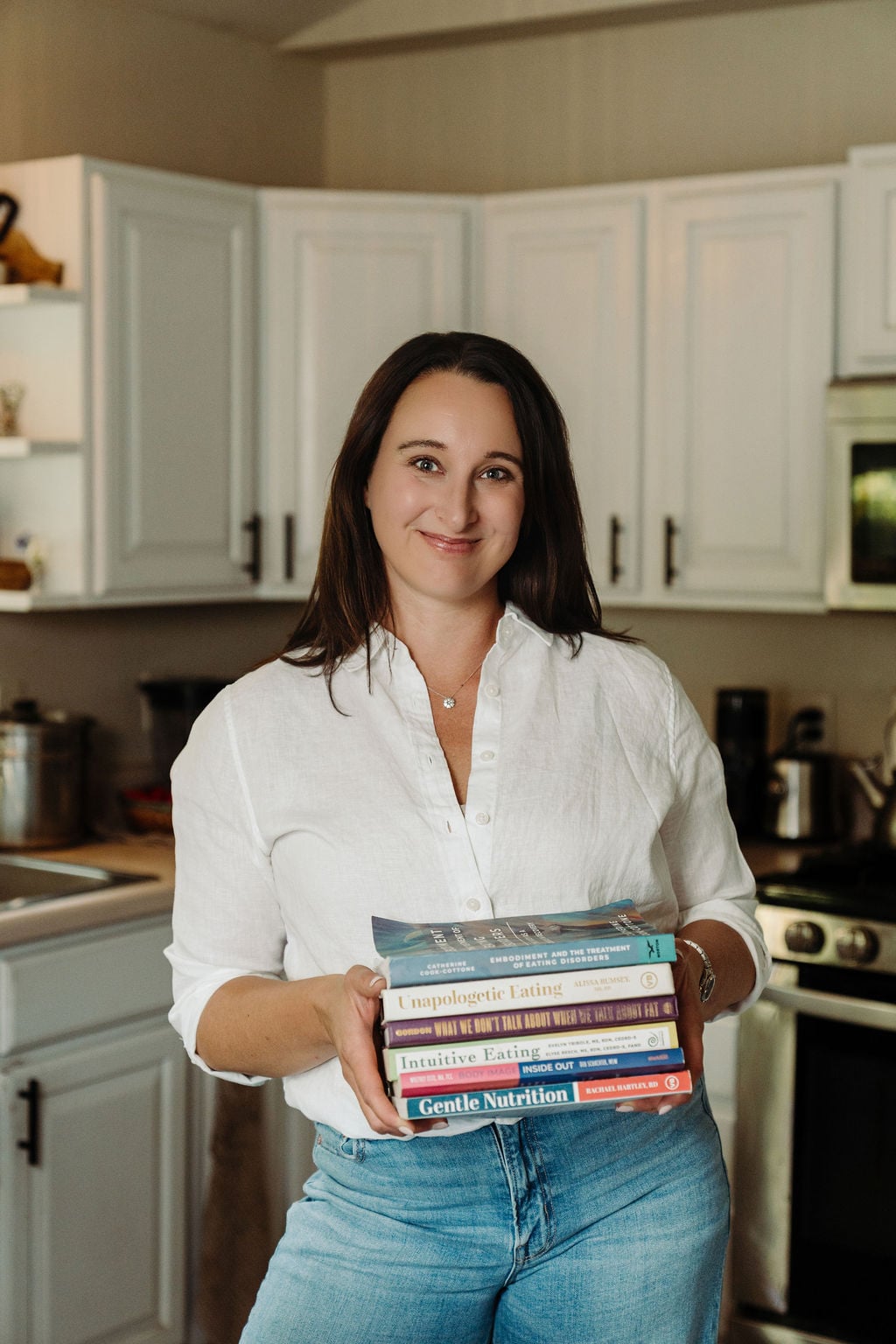 Stephanie McKercher in her kitchen with a stack of food and non-diet nutrition books.