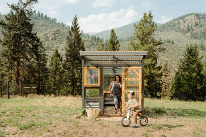 Stephanie McKercher standing in front of her Colorado greenhouse while her son rides by on a bicycle.